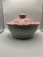 Front view of ceramic baking dish with gray base and pink textured lid with flower-shaped handle.