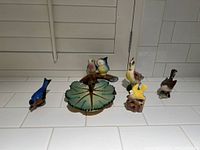 Seven ceramic bird figurines displayed on a white surface along with a green leaf-shaped decorative dish.