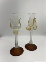 Pair of frosted glass candle sticks with twisted stems and flower-shaped tops, standing upright with brown bases.