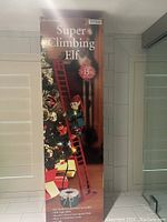 Box front showing 'Super Climbing Elf' with an image of the elf climbing a red ladder near a Christmas tree with gifts and ornaments.