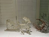 Photo showing the glass Christmas sleigh, and two glass reindeer decorations arranged on a white tiled surface.