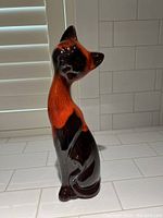 Tall, glossy ceramic cat figurine primarily red and black colors with stylized, elongated neck.