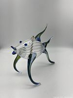 Angled side view of the glass fish sculpture showing ribbed body and three supporting fins with blue and green coloring