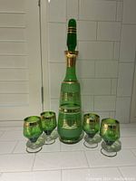 Full view of green glass decanter with stopper and four matching glasses with gold decoration.