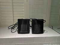 Front view of two black mini space heaters showing their front mesh grills and attached power cords.