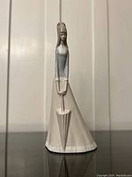 Single photo showing one of two identical Miquel Requena porcelain figurines depicting a woman in a long gray and white dress holding a closed umbrella.