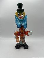 Front view of colorful Murano glass clown figurine with green top hat, blue collar, and red buttons.