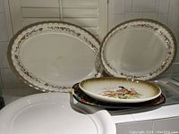 Four porcelain platters stacked and displayed showing floral, gold trim and pheasant nature design.