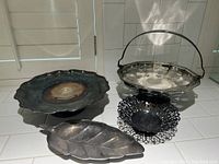 Photo of all four silverplate items displayed together: round cake stand, handled basket, small pierced dish, and leaf-shaped tray