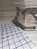 Photo of a porcelain square vase with floral design in pink, grey, and green, displayed beside a handwritten calendar.