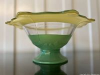 Side view showing green pedestal base with embossed pattern and clear bowl with yellow scalloped rim, visible cracks on glass