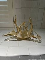 Angled side view of the hand blown glass dish showing the tripod base and upward abstract loops in amber glass.