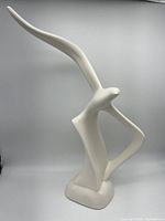 White abstract bird sculpture with smooth rectangular base photographed against white background.