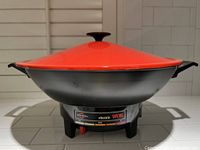 Electric wok with red lid on base unit showing control panel.