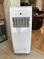 Full front view of white portable air conditioning unit standing on a tiled floor next to a wall corner.