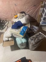Stack of bedding items including pillows, blankets, and towels on a chair and floor in unfinished basement