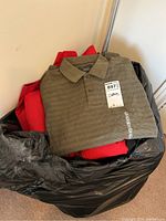 Olive green polo shirt on top of black bag filled with other clothing