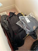 Large bag of assorted black clothing items including pants and tops, some packaged in plastic, with sizes labeled 36/L.