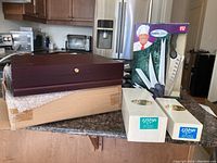 Photo showing two boxed Elypsis 5-piece cutlery sets and a brown wooden flatware case with additional cutlery and a boxed knife set labeled The Ultimate Series by TV.