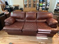 Front view of brown faux leather 3-seat sofa with plush cushions and padded rounded armrests.