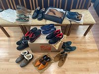 Overall view of approximately 13 pairs of men's and women's shoes in various styles and colors, arranged on chairs and floor.