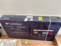 Front view of sealed Sansui TV box showing brand, model, Android TV, and 55" LED Smart UHD TV labeling.