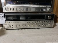Front view of Sansui receiver stacked below another audio component showing power switch, display window and control knobs