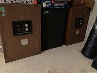 Three Sansui SP-3500 speaker cabinets on concrete floor showing rear panels and one front grill behind.
