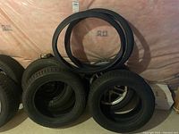 Photo showing multiple tires stacked, including two black bicycle tires leaned against a wall.