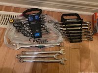 Overview photo showing two Mastercraft Maximum wrench sets side by side on floor; left set is metric flex-head ratcheting wrenches (7 pieces) and right set is standard ratcheting wrenches (7 pieces). Several loose combination wrenches also visible.