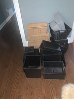 Overview of all storage boxes, showing three wicker and multiple black faux leather boxes on floor near wall.
