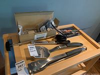 Napoleon BBQ tongs and spatula with a metal grater and Napoleon Grill Master recipe book on wooden surface.