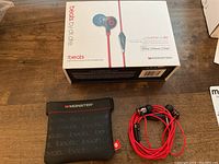 Beats by Dr. Dre iBeats headphones with red cable, black earbuds, inline mic, black Monster branded carrying pouch, and product box.
