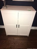 Front view of white wood cabinet showing two double panel doors with silver handles and flat top surface.