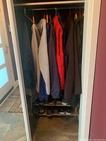 Closet space showing hanging men's coats and jackets with shoes on a two-tier wooden shoe rack at the bottom.