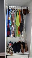 Wardrobe with hanging men's shirts in stripes, plaid, solids, and dark vest. Shelves below with multiple pairs of shoes including sneakers and slippers.