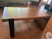Wood and metal coffee table with rectangular wooden top and two solid wood panel legs with two black metal rectangular legs.