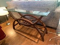 Side view of glass top and curved wooden base with intersecting ovals and wooden slatted shelf below.