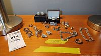 Overview of men's jewelry lot showing multiple rings, cufflinks, bracelets and a tie pin laid out on a wooden surface between two silver lamps.