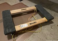 Top-down view of the wooden Milwaukee dolly showing the carpet pads and wooden frame with central handle cutout.