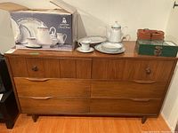 Full view of the wooden dresser showing six drawers, some scratches and a tea set placed on top (contents not included).