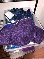 Top view of plastic bin filled with quilting fabrics, showing a prominent purple floral fabric on top.