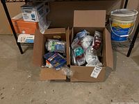 Boxes containing assorted small hardware items, light bulbs, and painters plastic sheets.