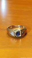 Front view of ring on wooden surface showing oval blue stone and gold band