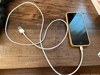 iPhone connected to white USB Lightning charging cable on wooden surface