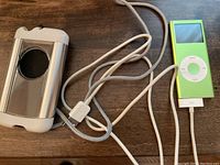 Apple iPod Nano with lime green color connected to a cable and next to a silver hard case.