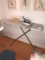 Ironing board with Grey and white patterned cover, metal X-shaped legs, showing the wooden tailor board and Black & Decker iron on top.
