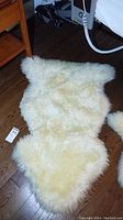 Full view of the cream colored lambskin rug on wooden floor showing irregular natural shape and fluffy pile.