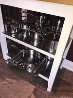 Three shelves of stainless steel cookware on white cart