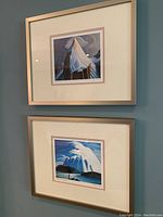 Two framed prints hanging on blue wall, one above the other, depicting mountain scenes.
